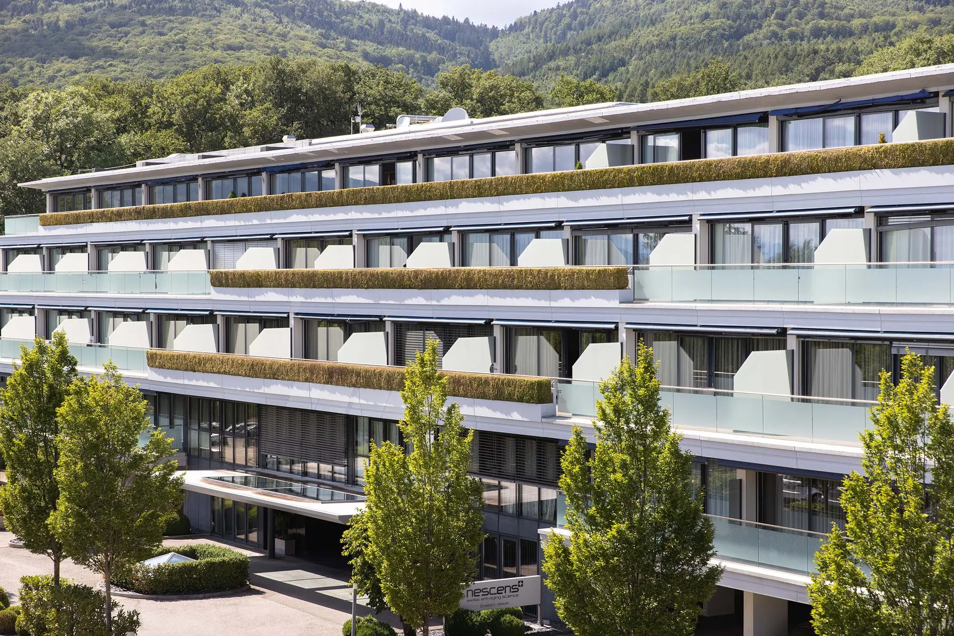 Modern spa facility exterior with lush greenery and mountain backdrop.