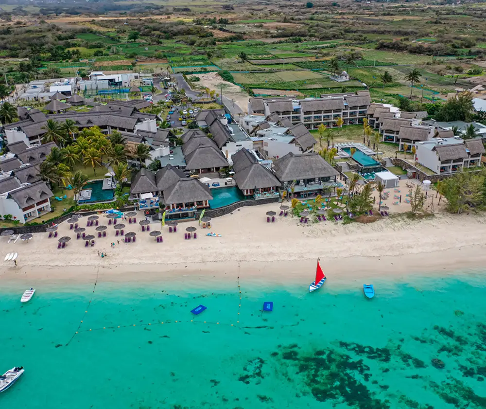 Aerial view of luxury beachfront resort with turquoise waters and red sailboat.