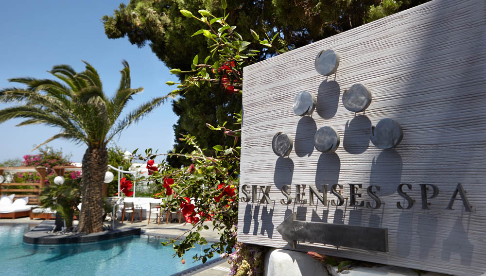 "Luxury spa poolside with palm trees and Six Senses Spa sign."