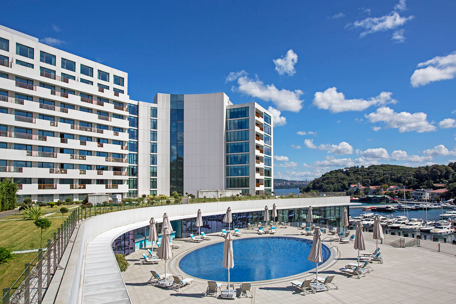 Modern luxury hotel with poolside relaxation area and scenic marina view.