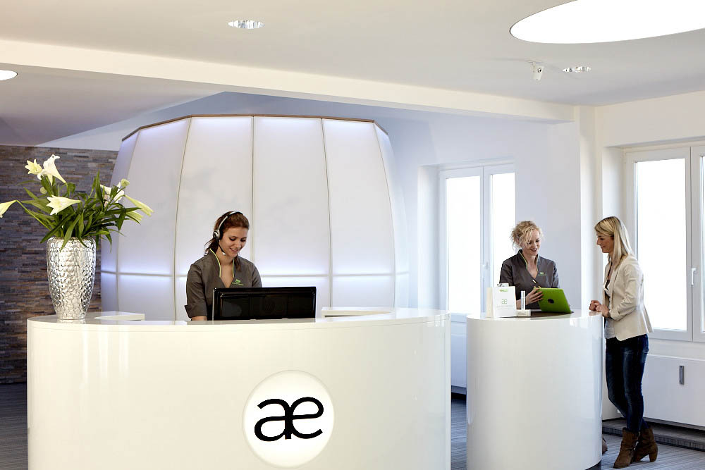 "Modern spa reception with sleek white desk and professional staff interaction."